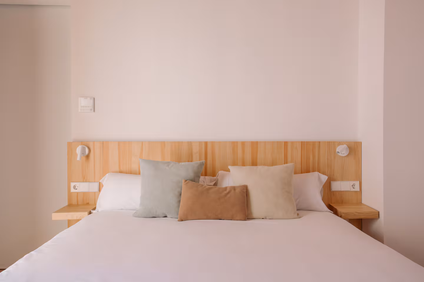 Cama de matrimonio con cabecero de madera clara y cojines en tonos tierra
