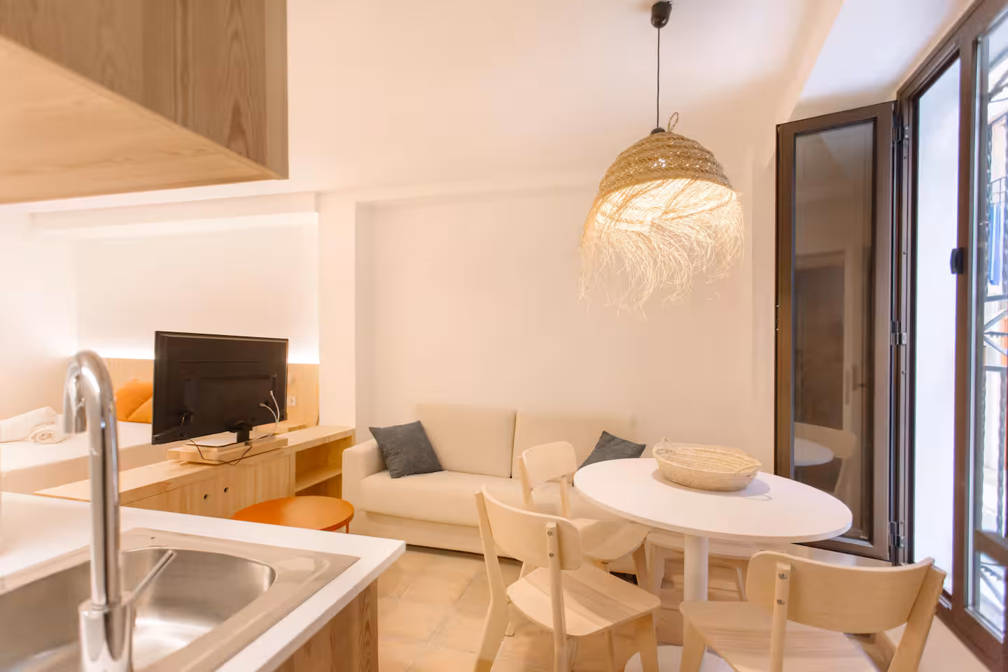 Cocina con fregadero y encimera abierta al salón, con el balcón al fondo