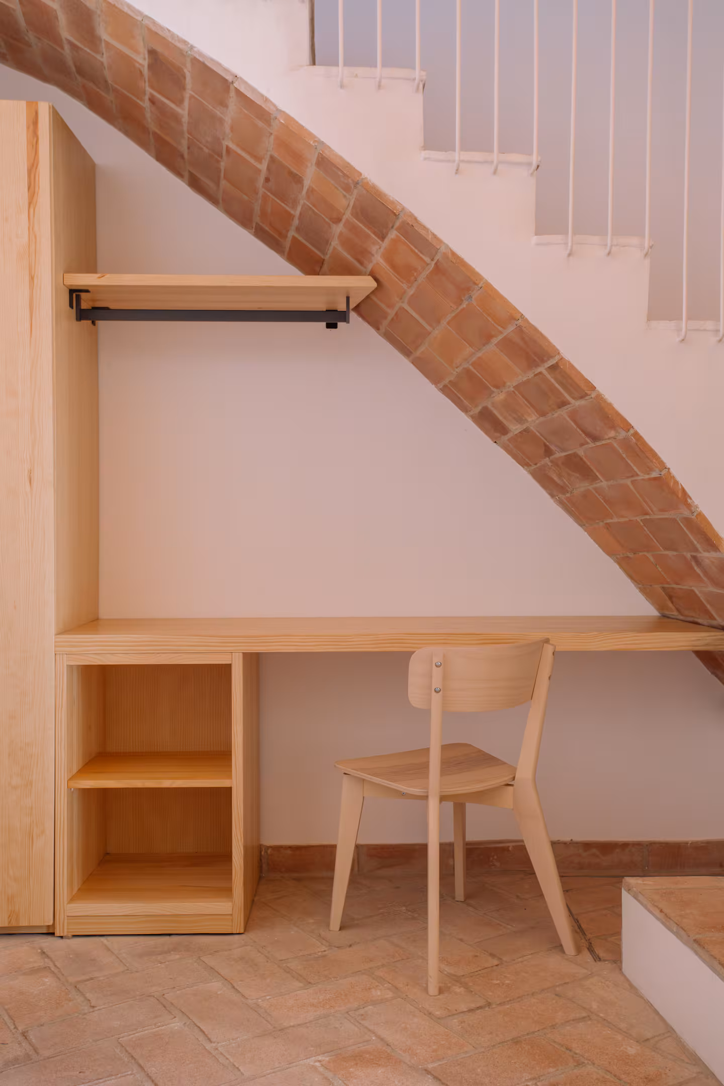 Escritorio de madera clara encajado bajo la escalera, con el arco de ladrillo visto